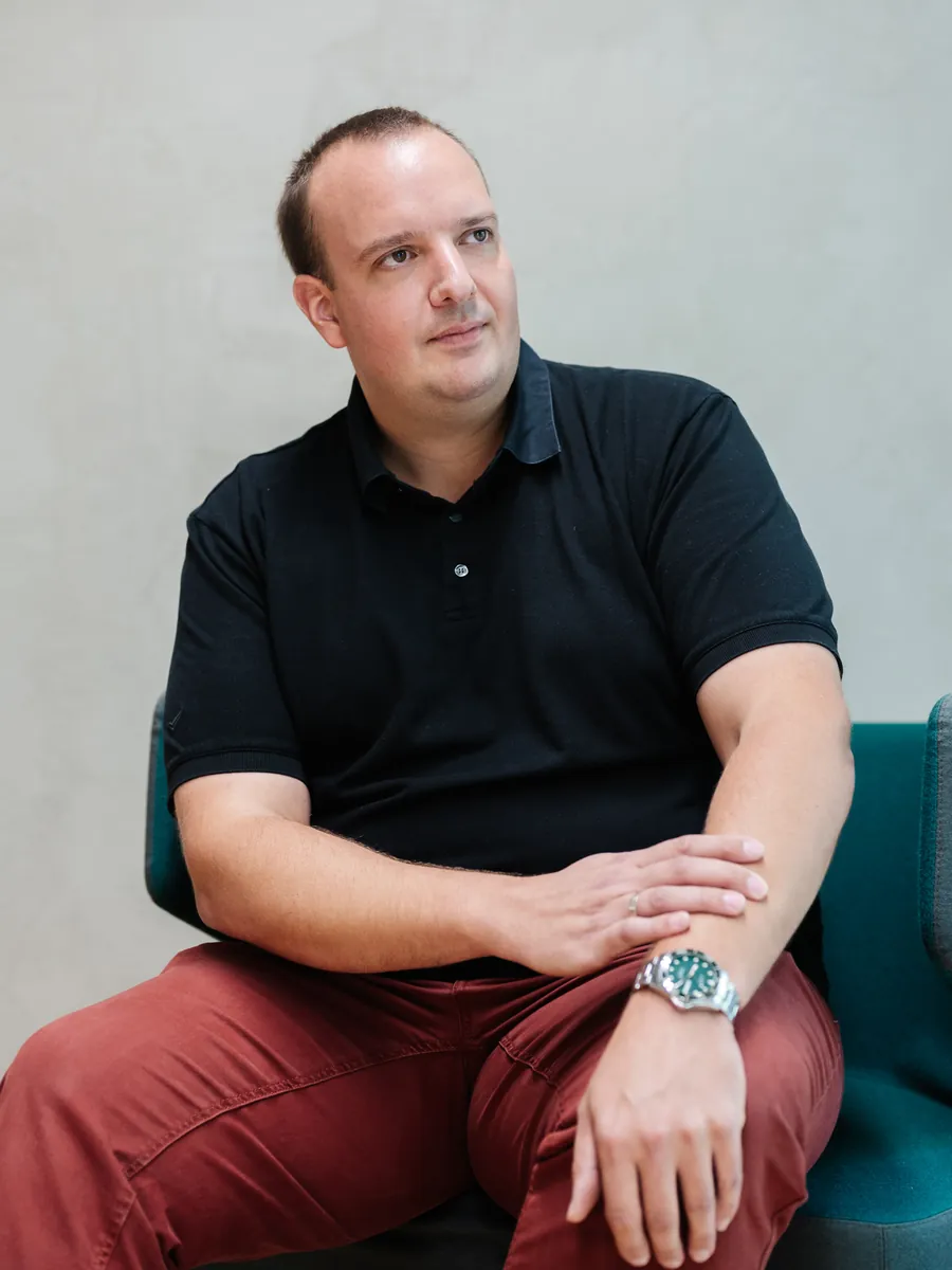 Geschäftsführer Fabian Becker sitzt in einem petrolfarbenen Sessel vor einer grauen Wand